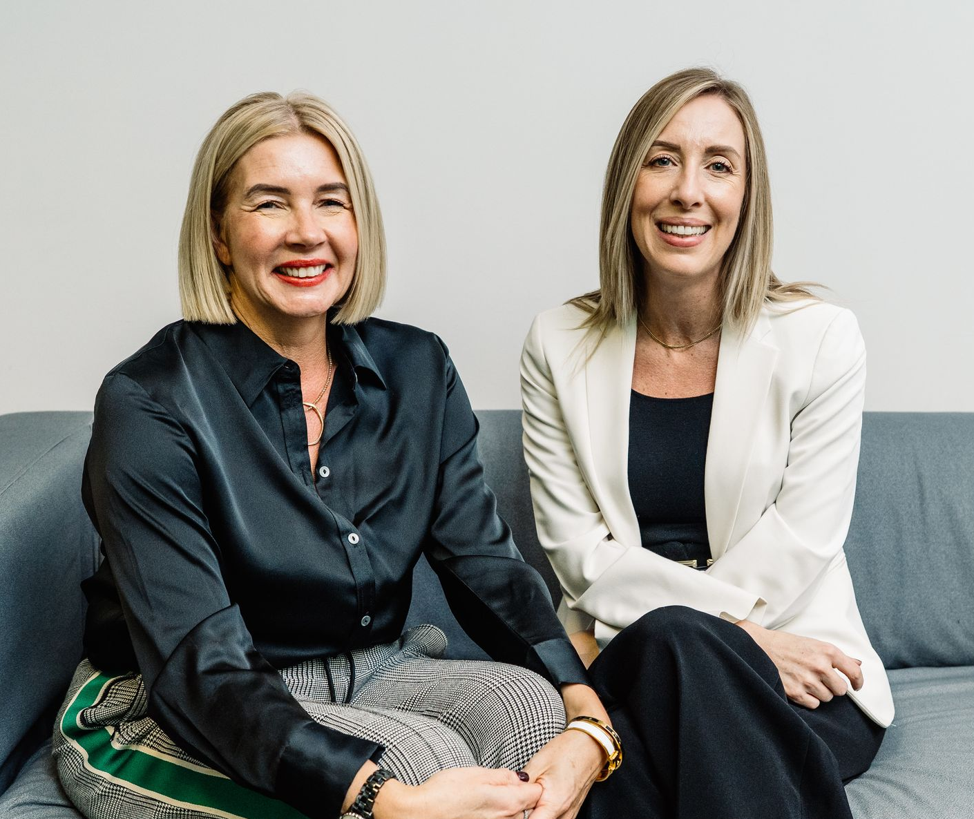 Two women are sitting next to each other on a couch and smiling.
