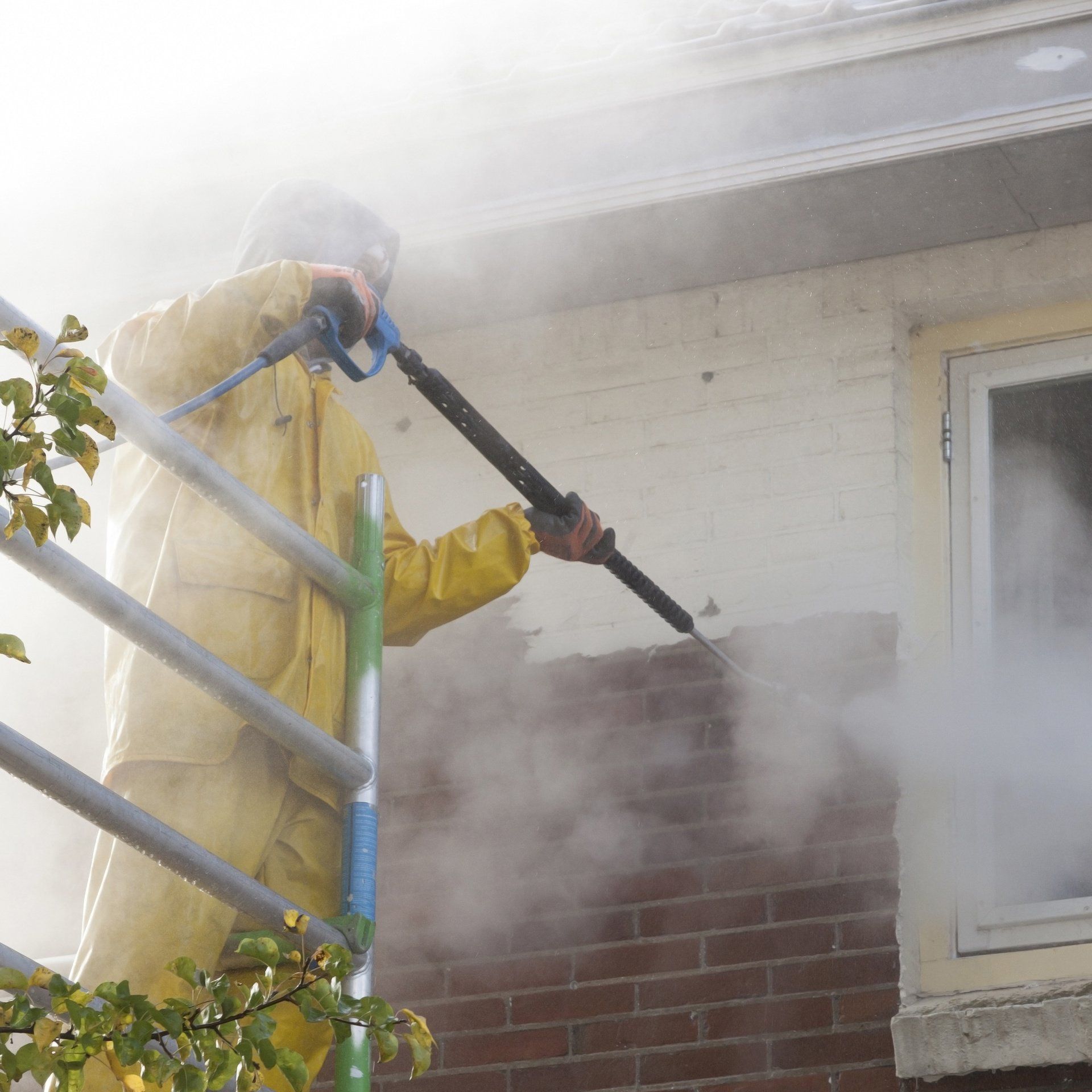 A man in a yellow jacket is spraying water on a brick wall