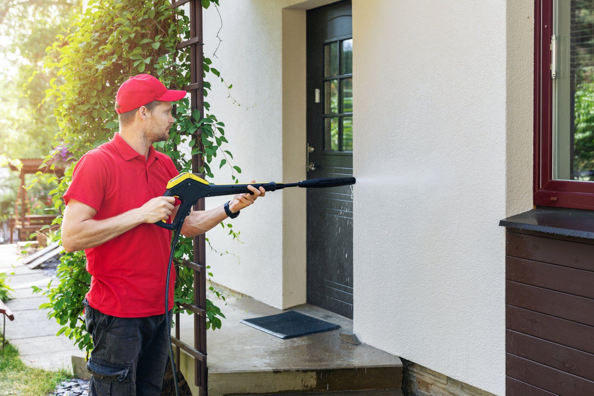 A man is cleaning the side of a house with a high pressure washer.