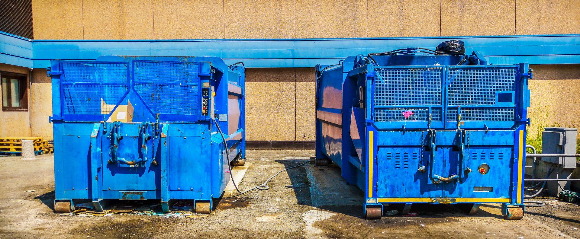Two blue dumpsters are parked next to each other in front of a building.