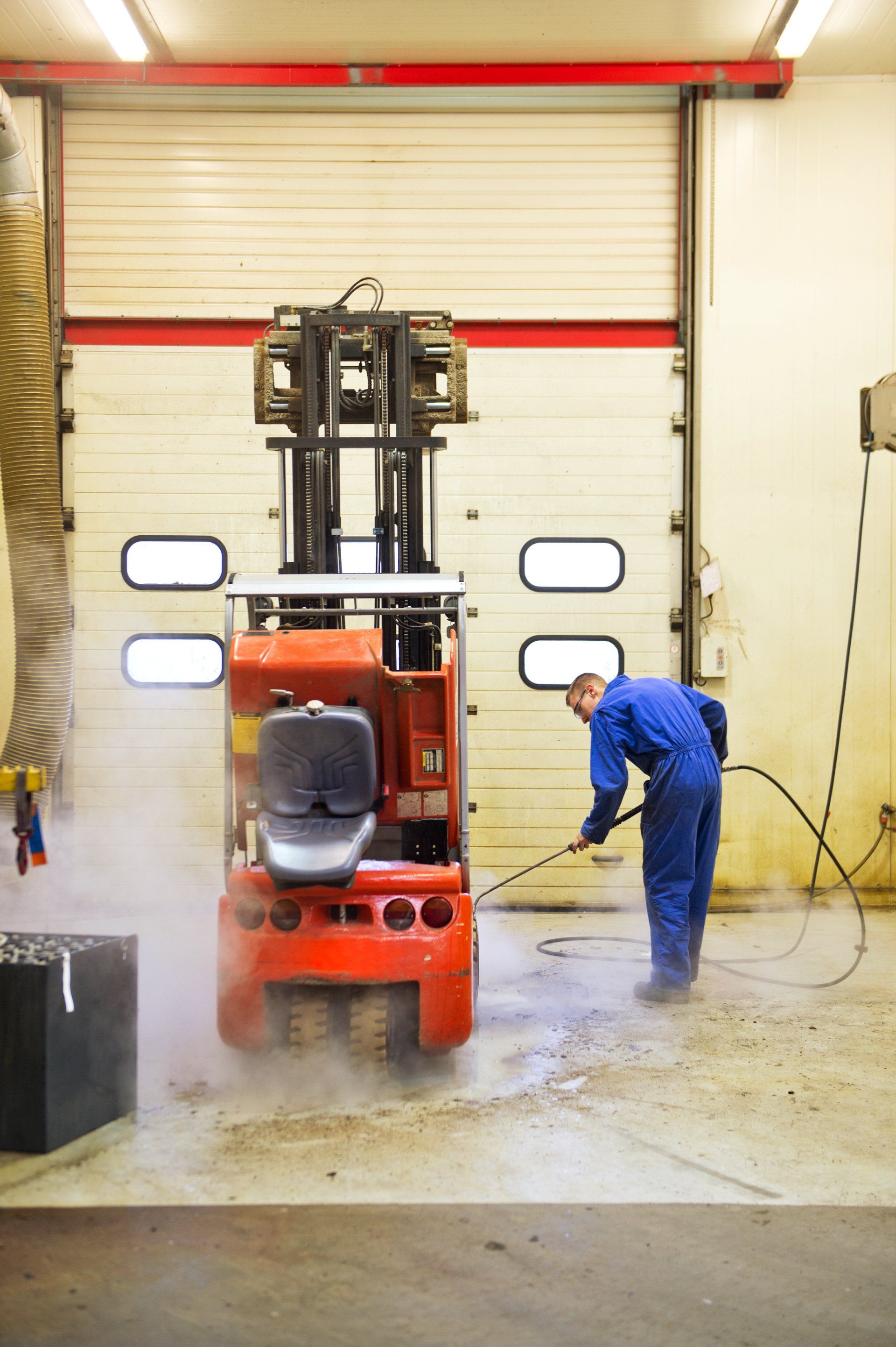 A man is cleaning a forklift in a garage.