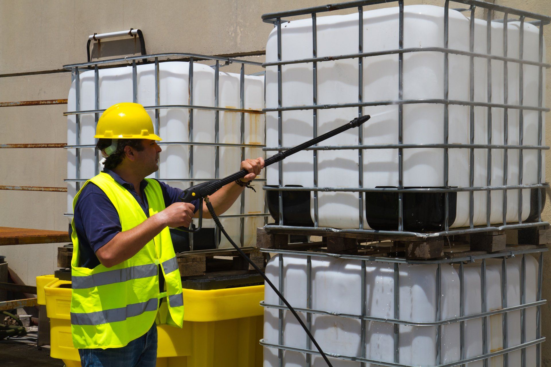 A man wearing a hard hat and safety vest is spraying a white container