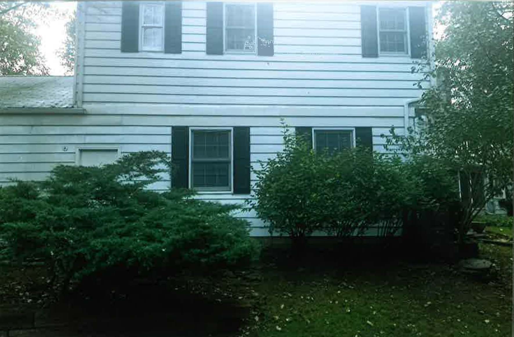 A white house with black shutters and bushes in front of it