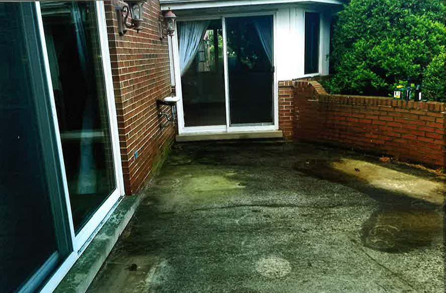 There is a patio in front of a brick house with a sliding glass door.