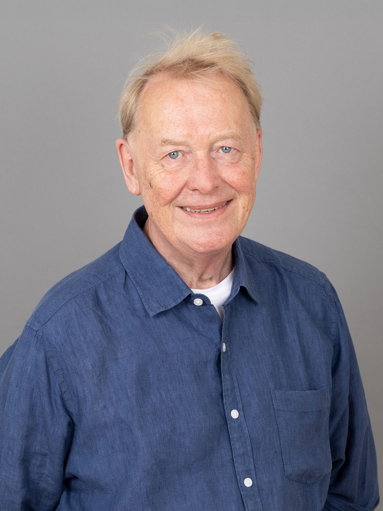 Lächelnder älterer Mann in einem blauen Hemd vor grauem Hintergrund.