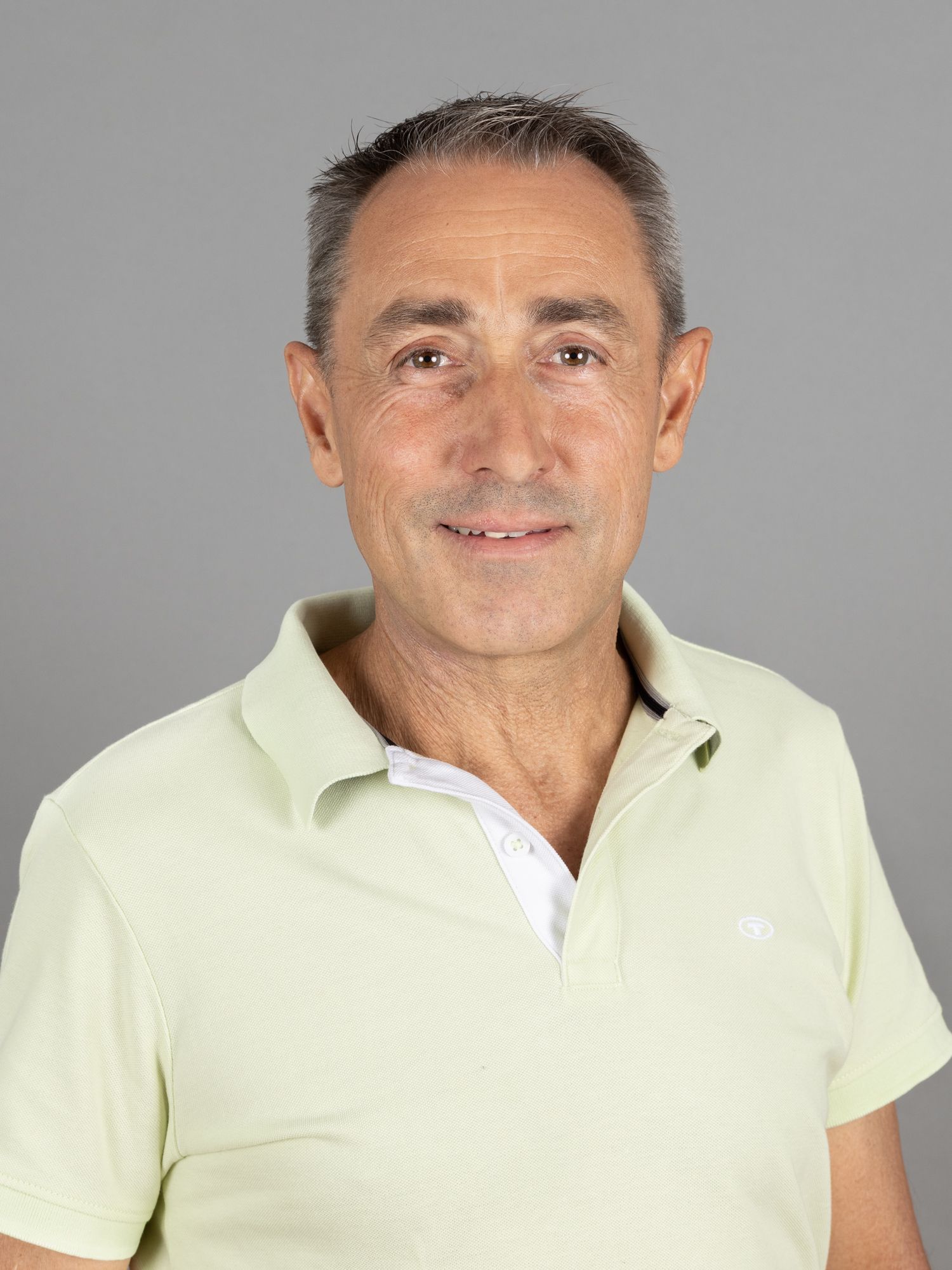 Ein Mann in einem hellgrünen Poloshirt lächelt und posiert vor einem grauen Hintergrund.