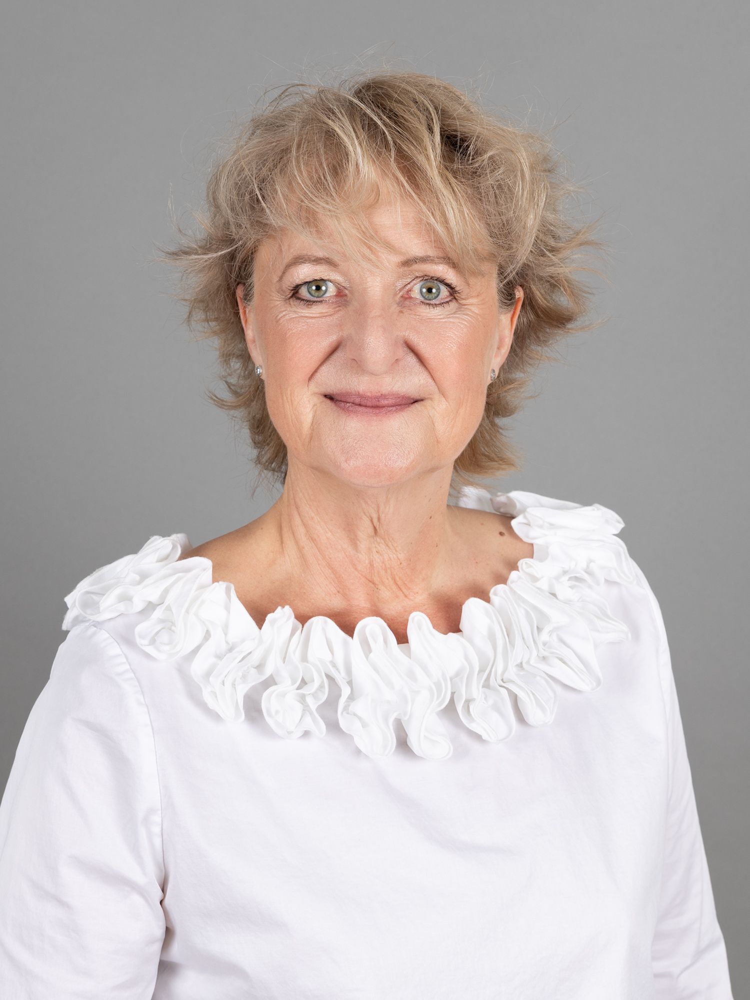 Frau in weissem Top mit Rüschenkragen lächelt in die Kamera.