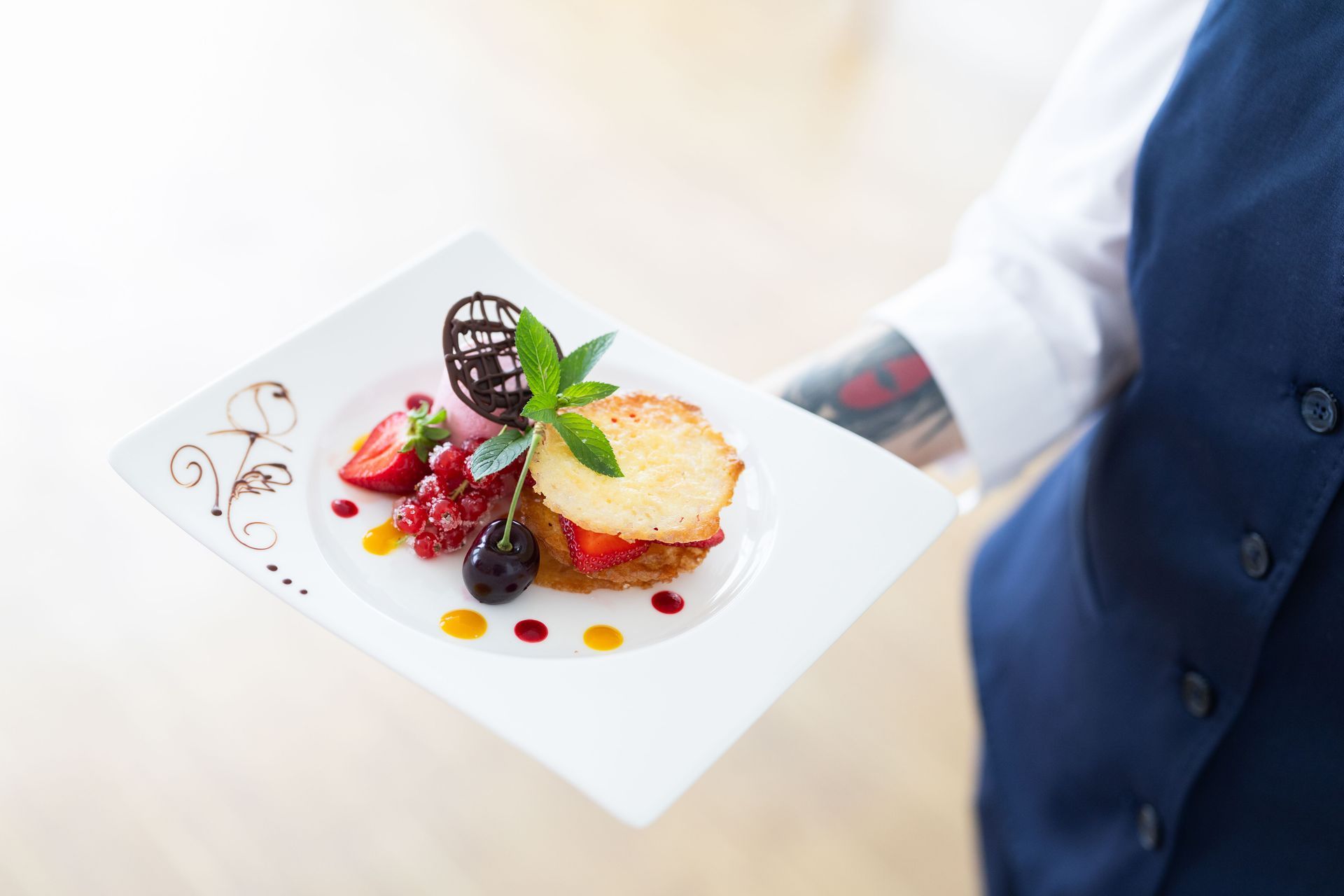 Eine Kellnerin hält einen Teller mit einem Gourmet-Dessert: Kuchen, Beeren, Schokolade und Minze.