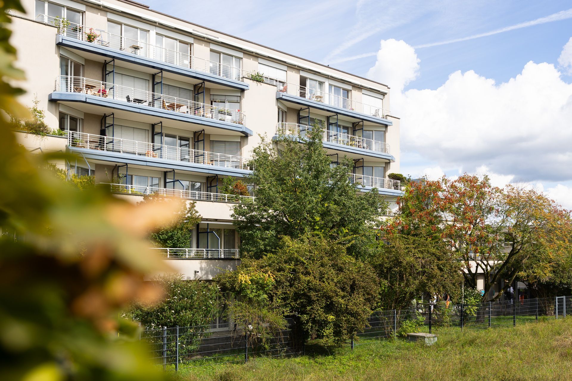 Wohnhaus mit Balkonen, Bäumen und blauem Himmel.