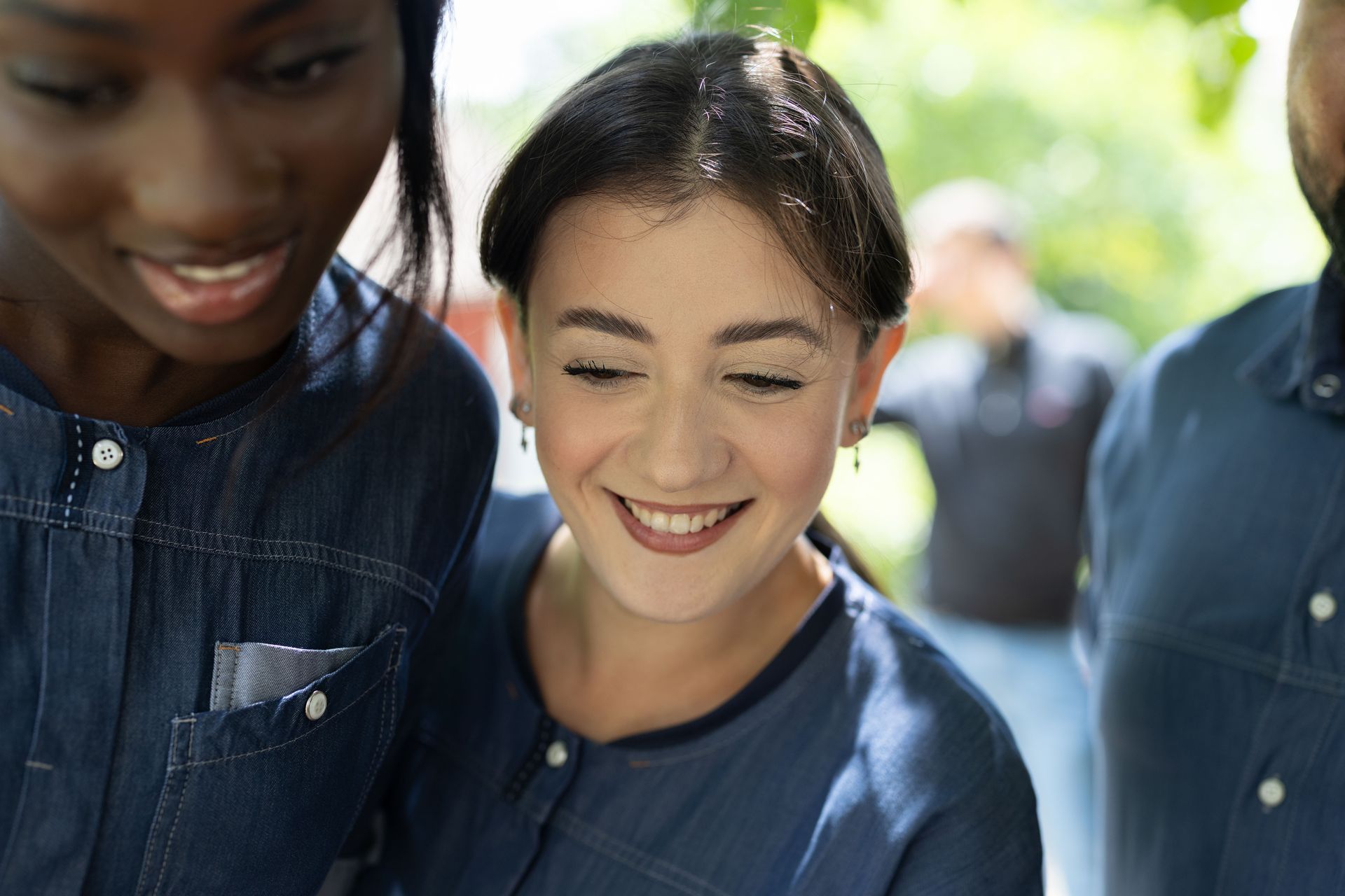 Drei lächelnde Personen, die nach unten schauen; draussen, sonnig.