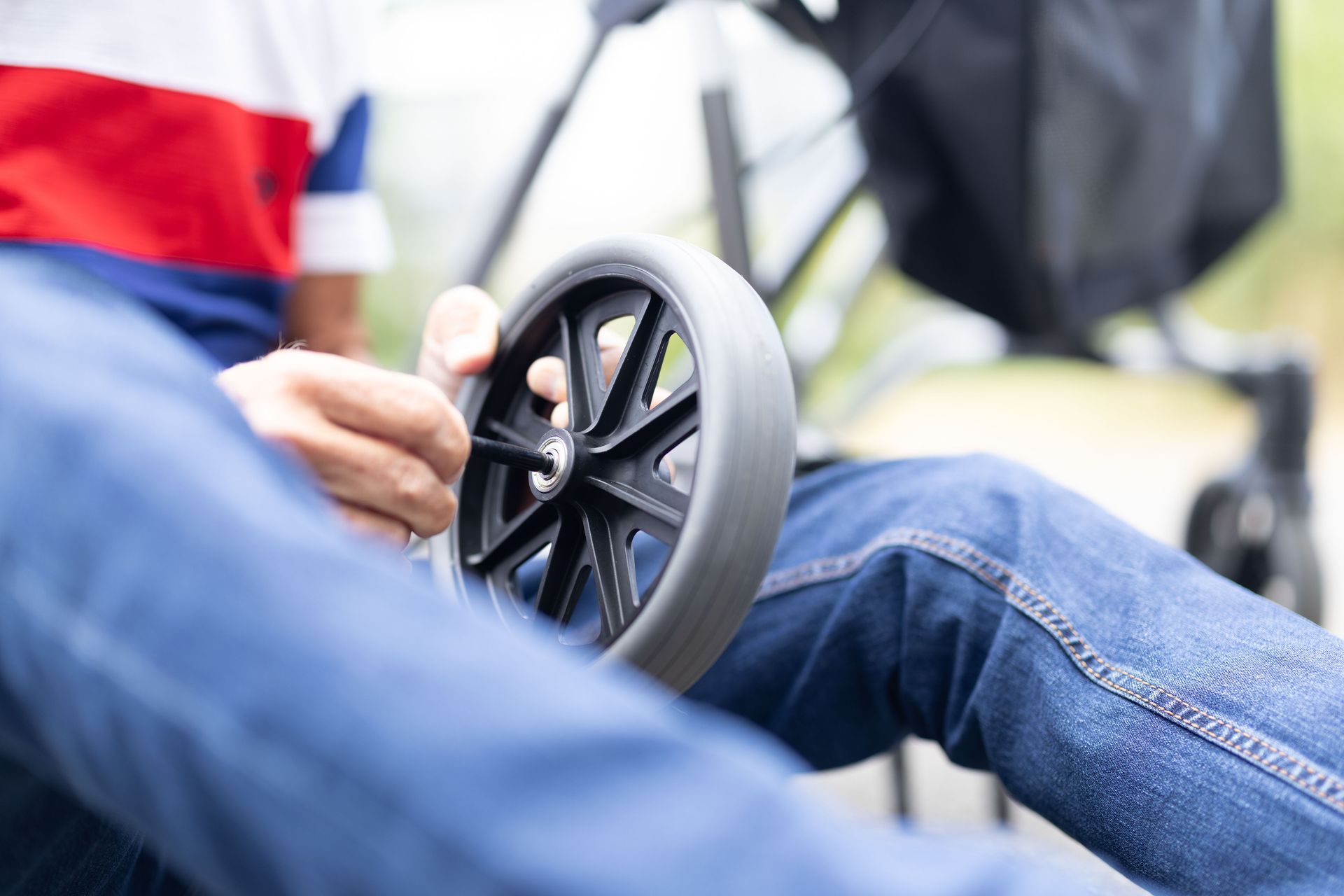 Person hält ein Kinderwagenrad, Nahaufnahme. Jeans, buntes Hemd, im Freien.