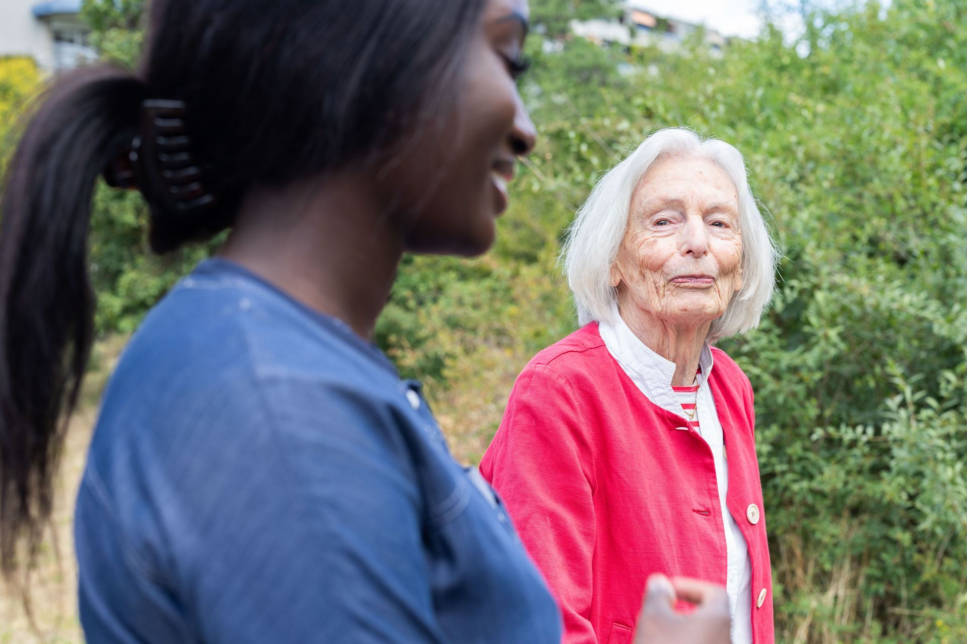 Junger und älterer Mensch im Freien, lächelnd, im Hintergrund Grün.