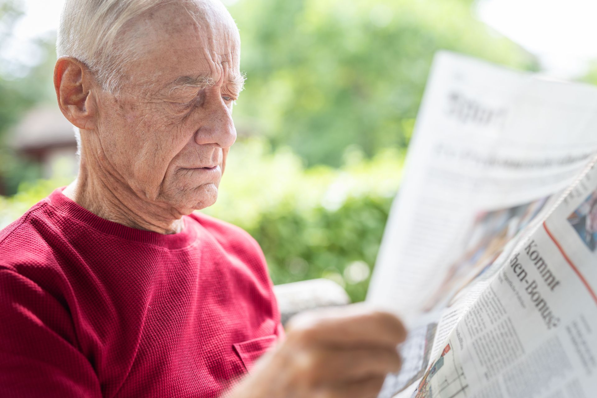 Ein älterer Mann in einem roten Hemd liest im Freien Zeitung.