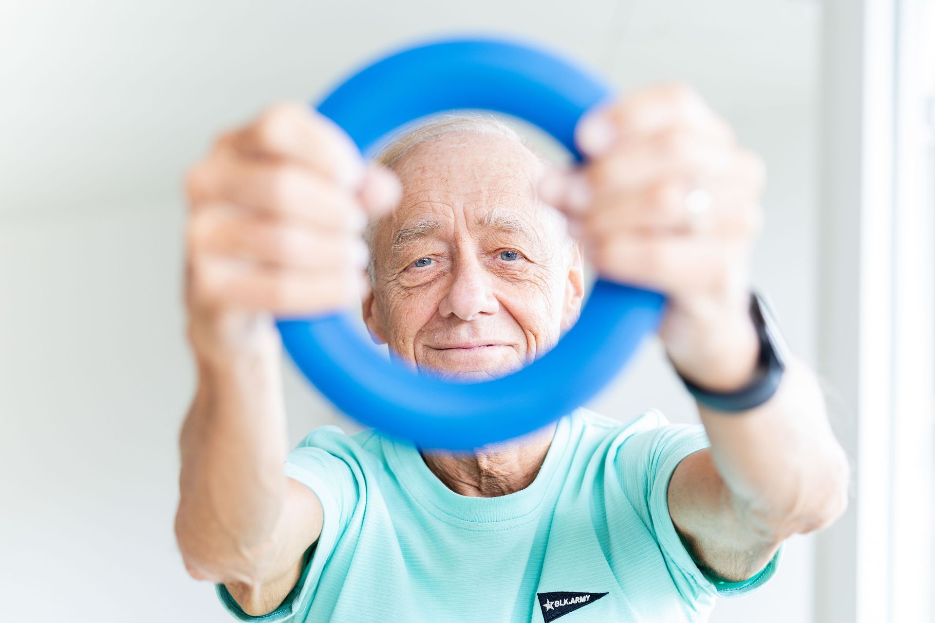 Älterer Mann, der einen blauen Fitnessring hält und lächelt.
