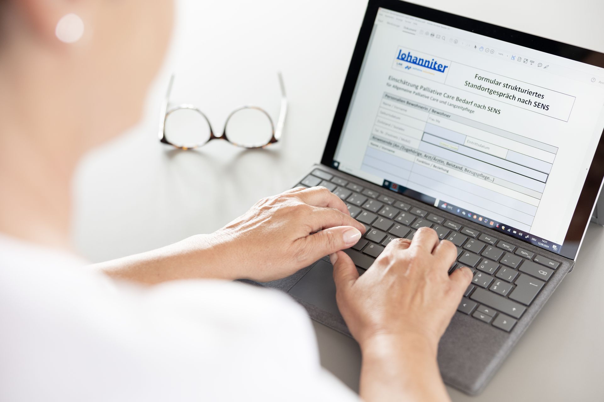 Eine Person mit Brille tippt auf einem Laptop; auf dem Bildschirm ist ein Dokument geöffnet.