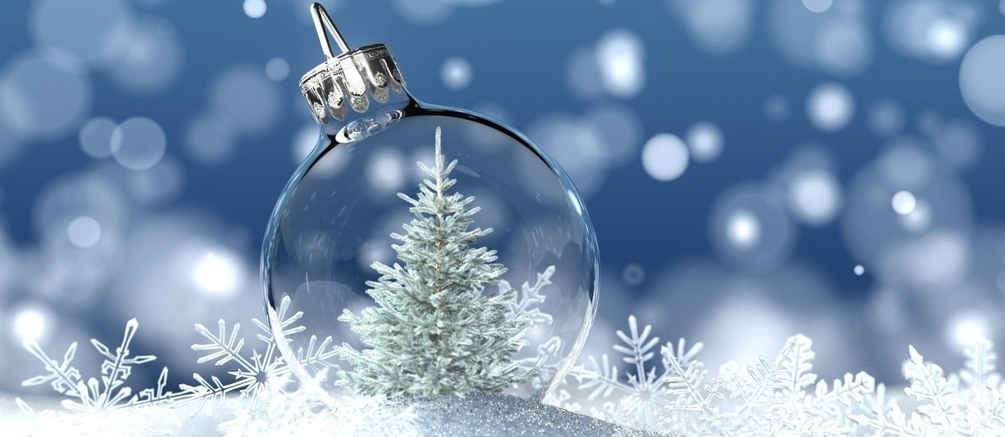 Eine transparente Weihnachtskugel vor lauem Hintergrund mit Schneeflocken