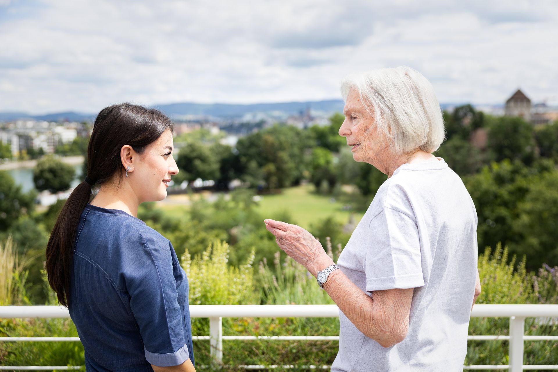 Eine Frau in Blau unterhält sich im Freien mit einer älteren Frau und blickt dabei auf Basel.