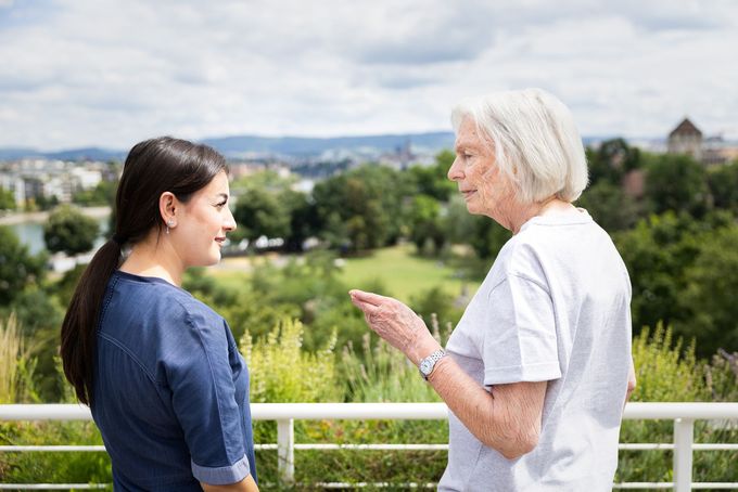 Eine Frau in Blau unterhält sich im Freien mit einer älteren Frau und blickt dabei auf Basel.
