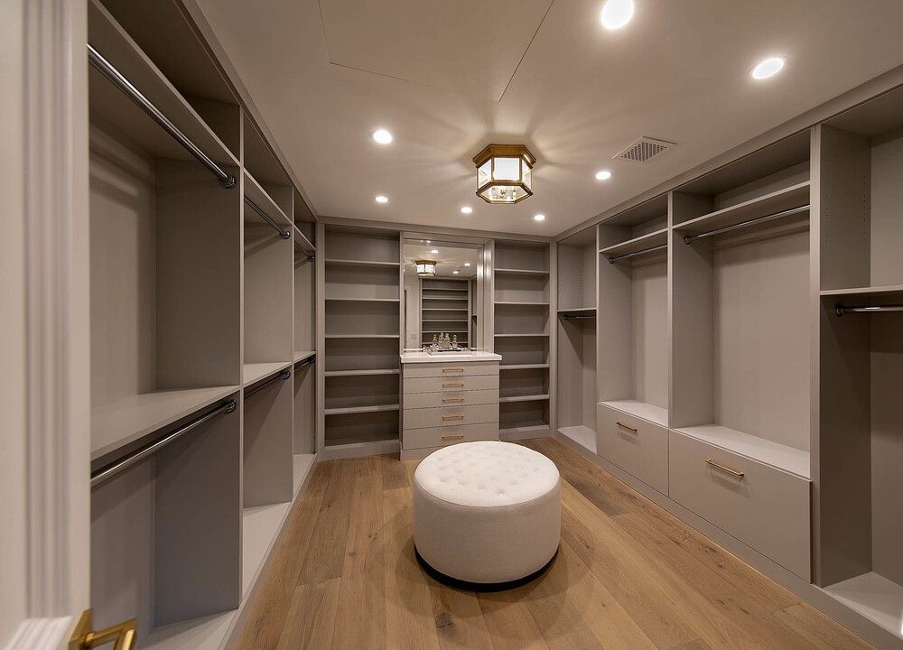 A large walk in closet with a white ottoman in the middle.