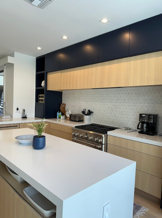 Modern kitchen with white countertop island, light wood cabinets, navy upper cabinets, and a stainless steel stove.