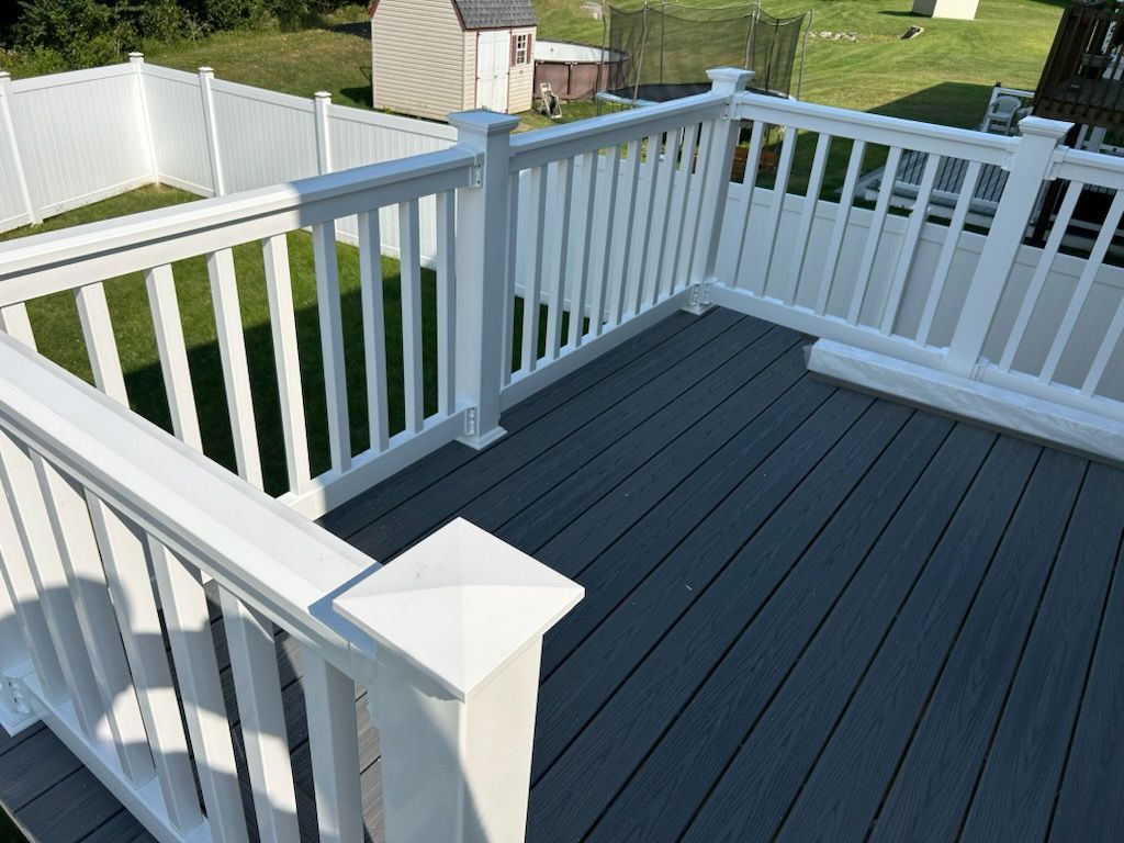 A white railing on a gray deck with a white fence in the background.