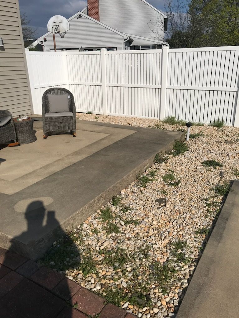 A white fence surrounds a patio with a chair and a table.