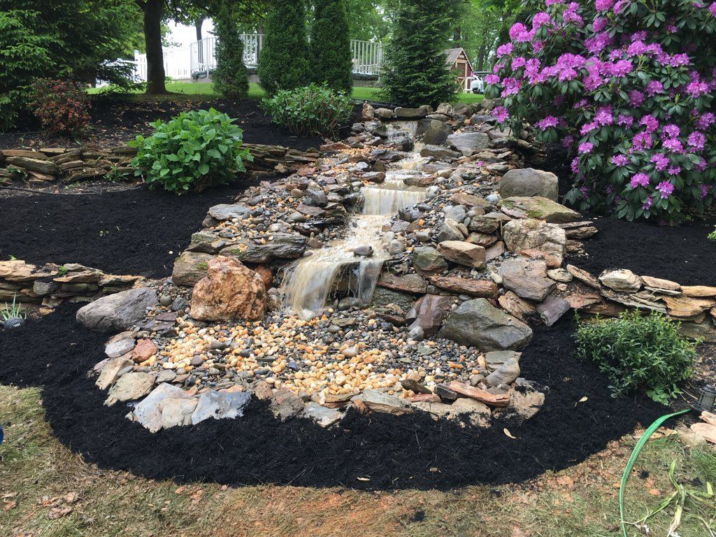 A waterfall is surrounded by rocks and flowers in a garden.