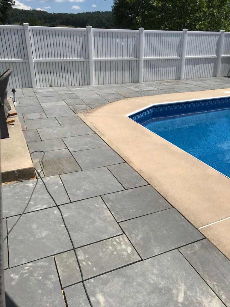 A swimming pool with a white fence and a patio in front of it.