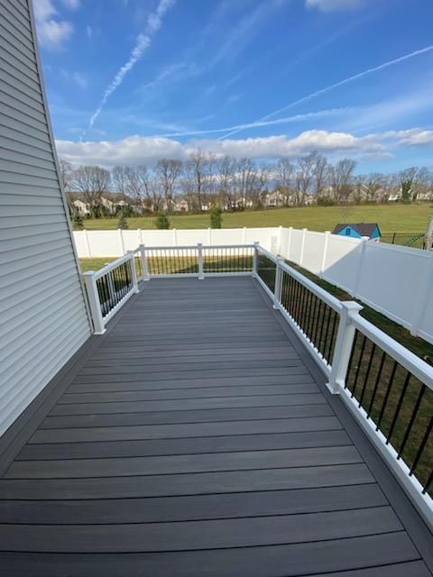 A large deck with a white railing and a fence in the background.