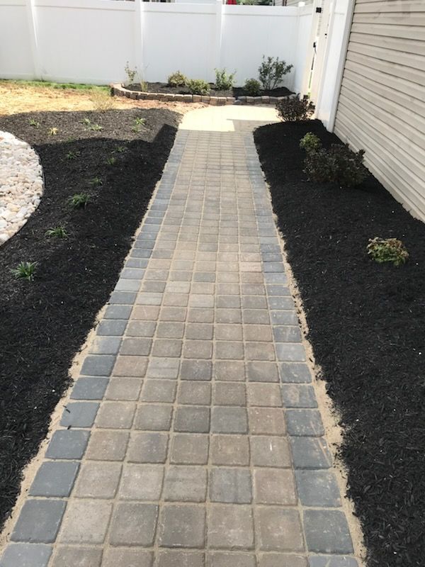 A brick walkway leading to a house with a white fence