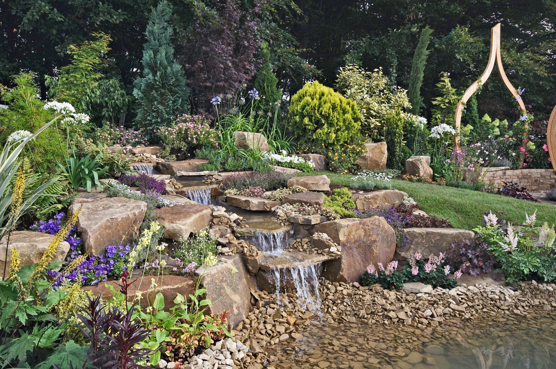 A Waterfall in a Garden With a Statue in the Background
