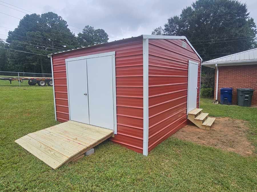 Red metal shed with white doors and ramp, next to a small set of wooden stairs.