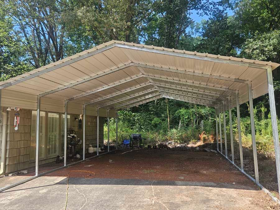 Carport with a beige metal roof and metal frame, on a gravel surface. 