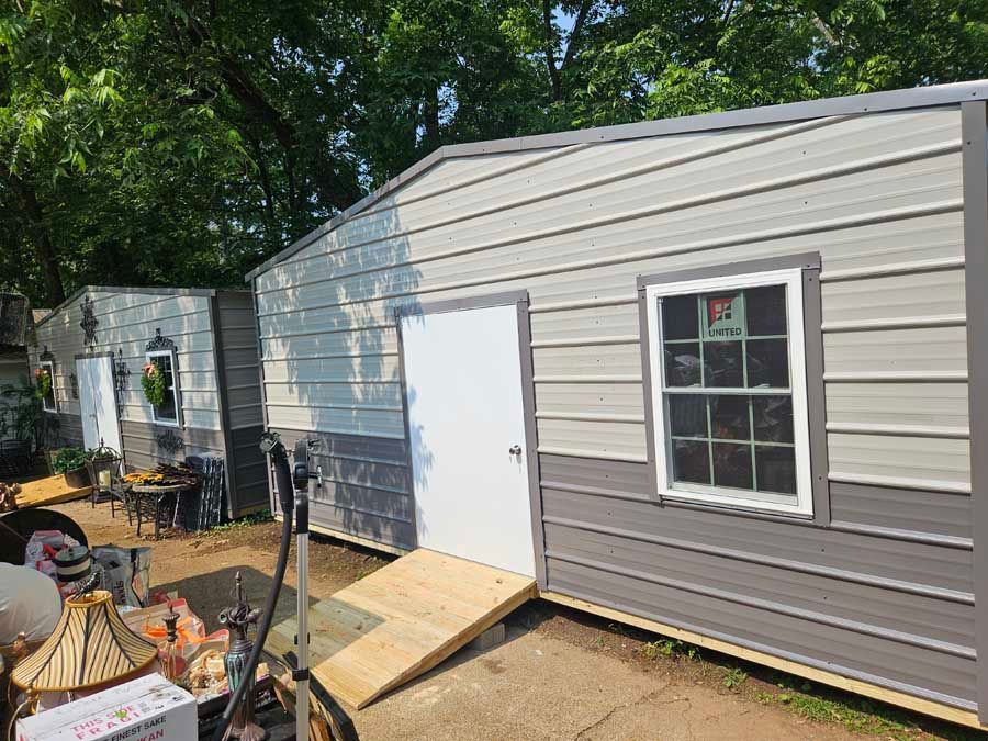 Metal sheds with gray and white siding, one with a ramp and window.