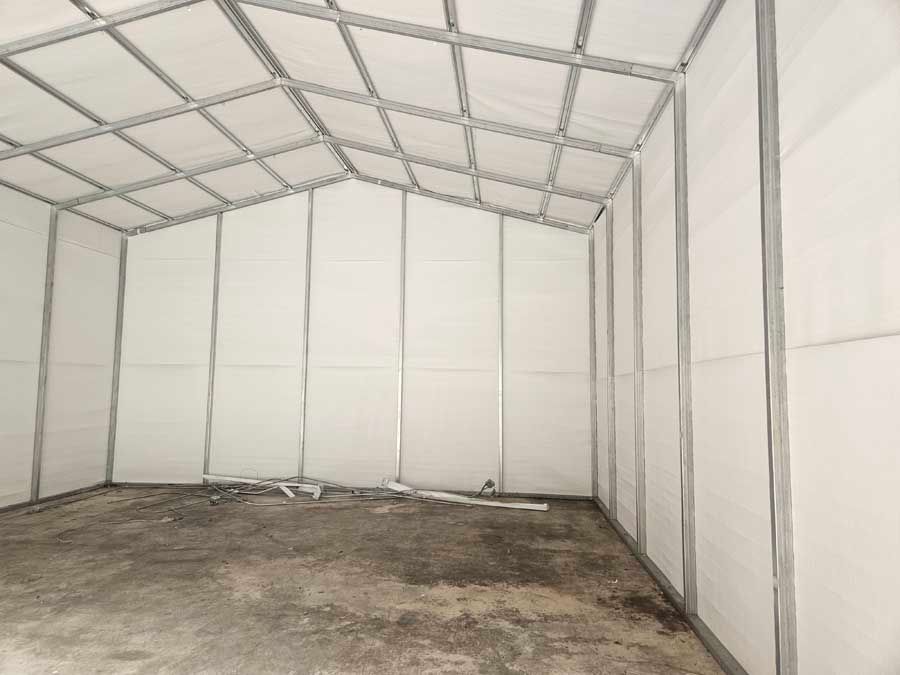 Interior of a white tent structure with a metal frame and concrete floor.