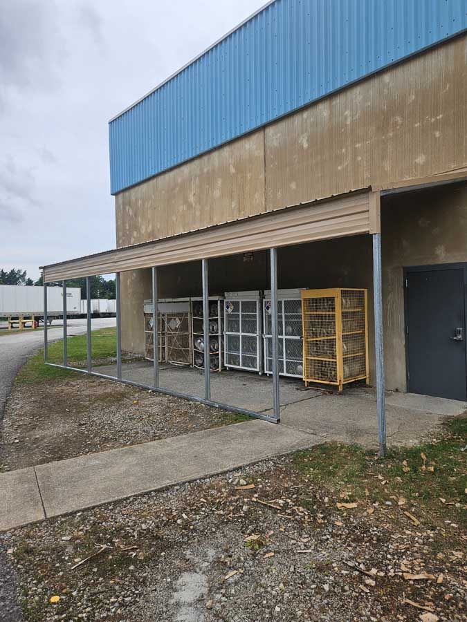 Outside a building, covered area with several metal storage cages on a concrete slab.