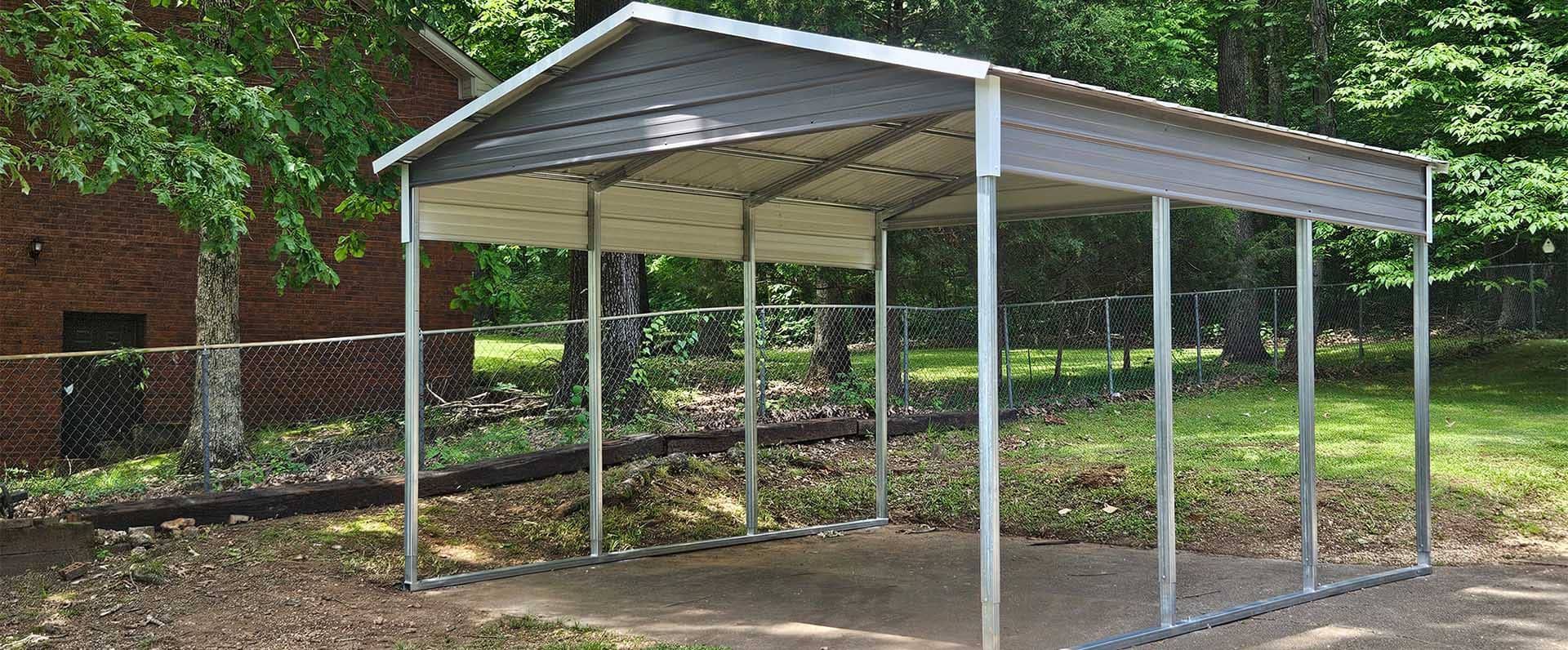 Metal carport in a yard with a concrete pad. Grey roof, silver posts, and lush greenery.