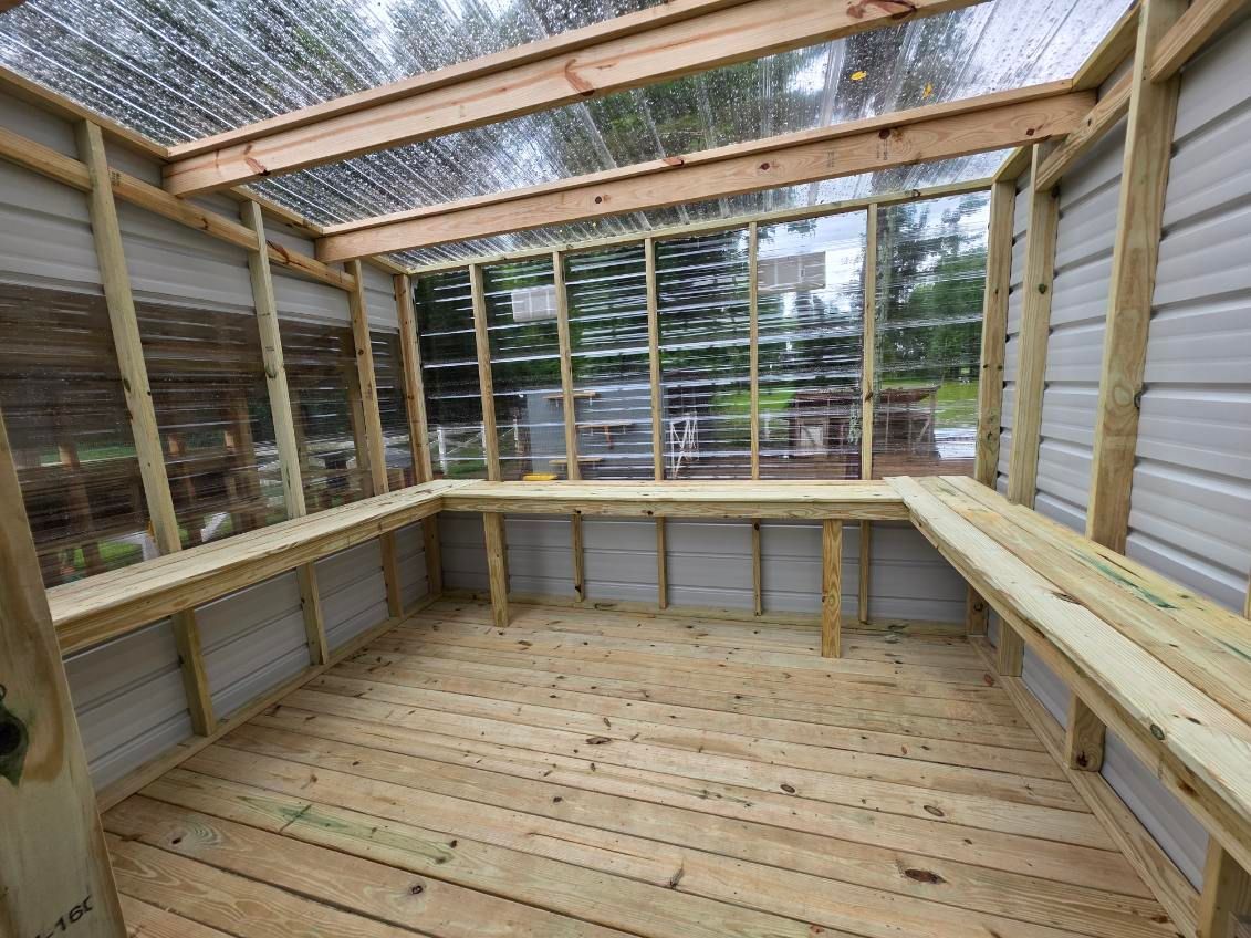 Empty wooden deck with partial walls and open roof framing under construction, overlooking trees.