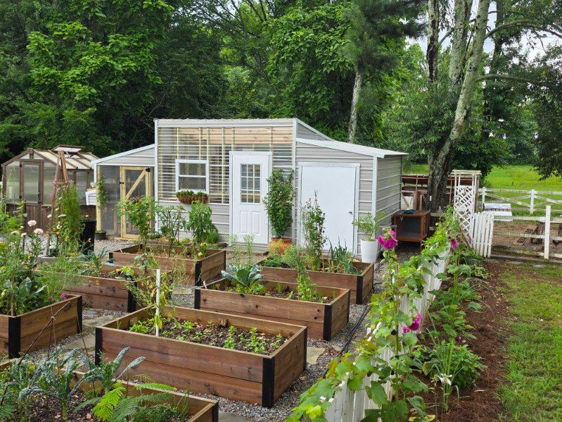 Community garden with raised beds and a white greenhouse surrounded by flowers and trees