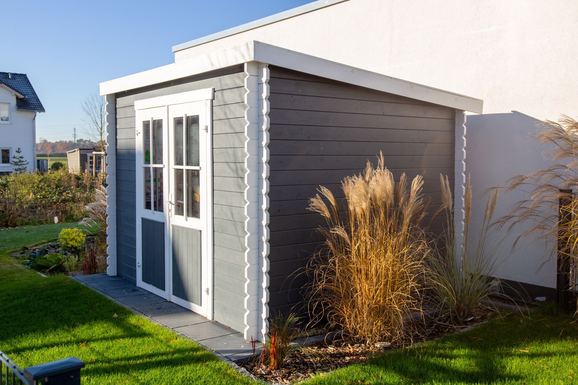 Gray shed with white trim and double doors; tall ornamental grass in front.