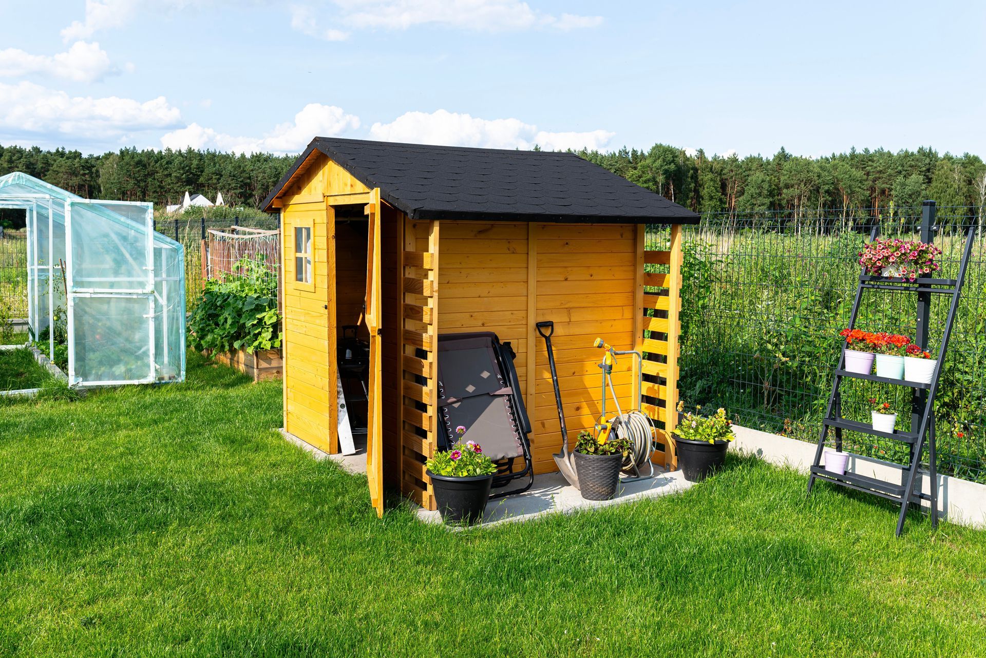 Wooden shed with open door, garden tools, and plants on a grassy lawn.