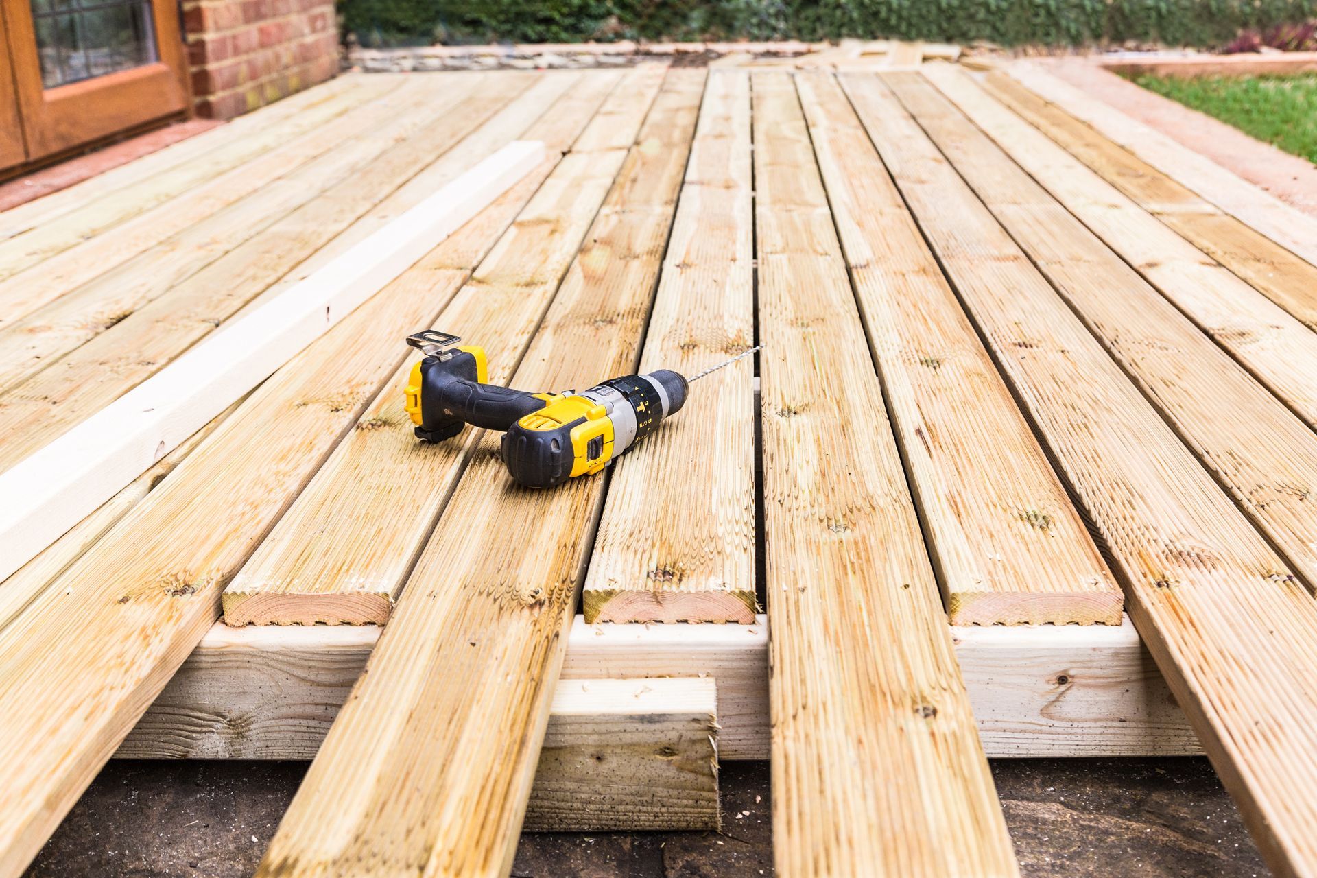 Wooden deck under construction, with a drill resting on unfinished planks.