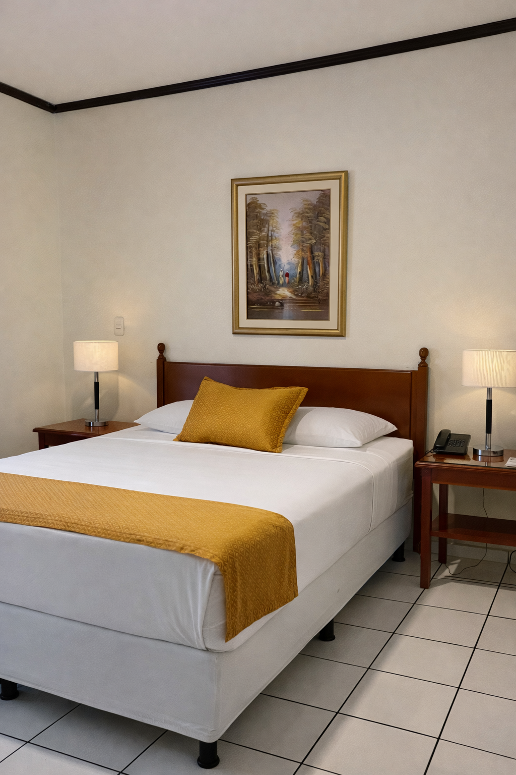 A hotel room with a queen bed featuring a mustard yellow runner and pillow, flanked by two lamps on wooden nightstands.