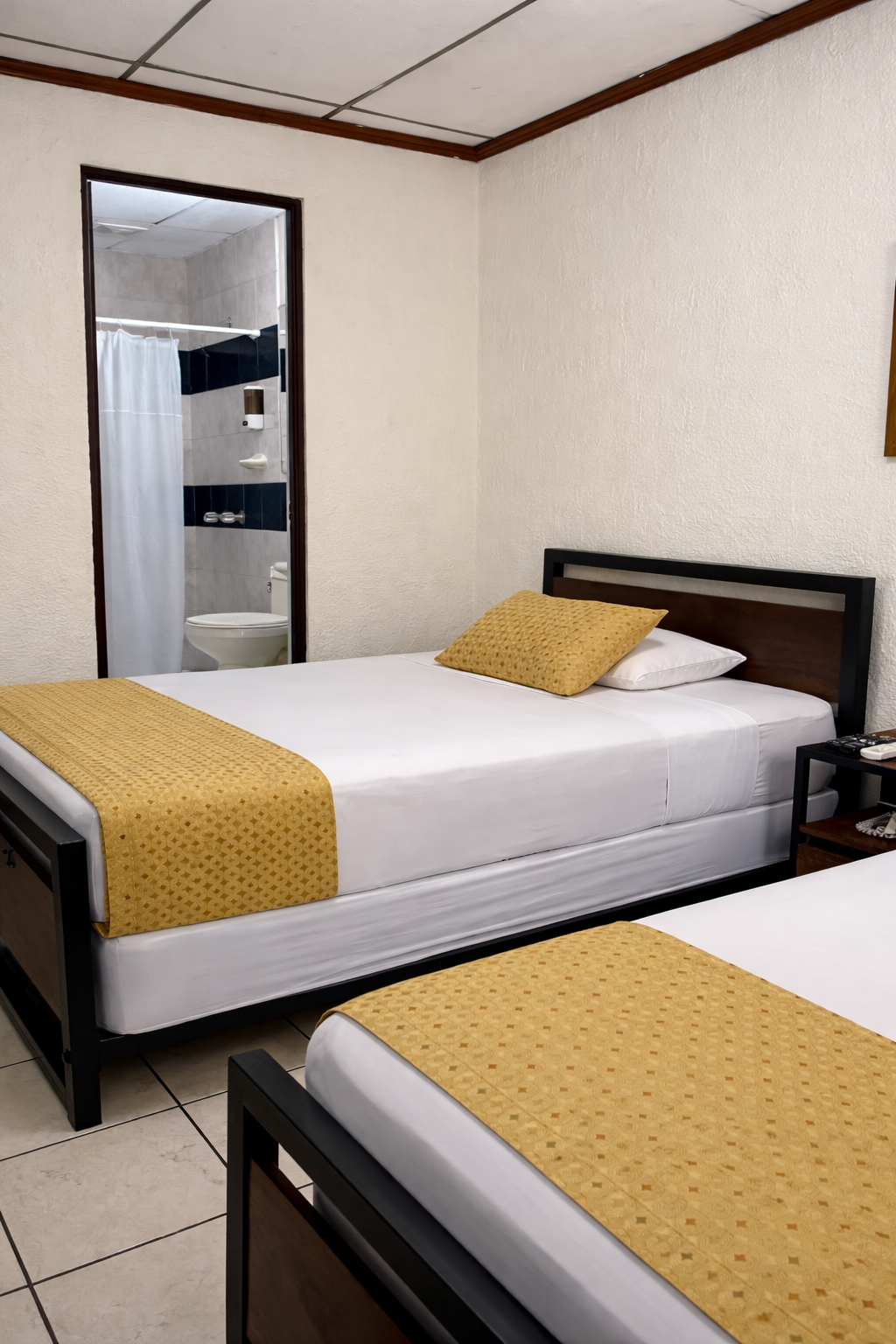 A hotel room featuring two beds with white linens and yellow runners, next to an open doorway leading to a bathroom.