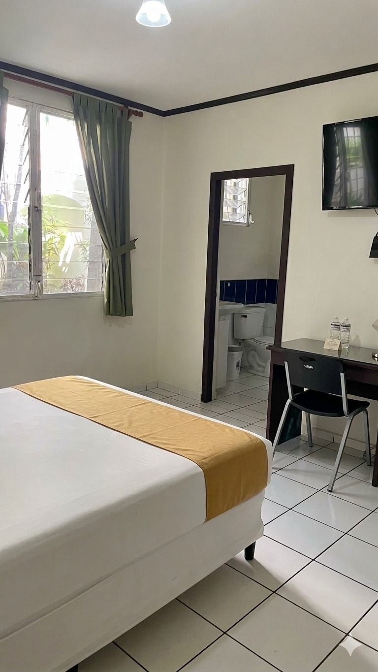 A bedroom with a bed featuring a gold runner, a desk with a chair, and an open doorway leading to a tiled bathroom.