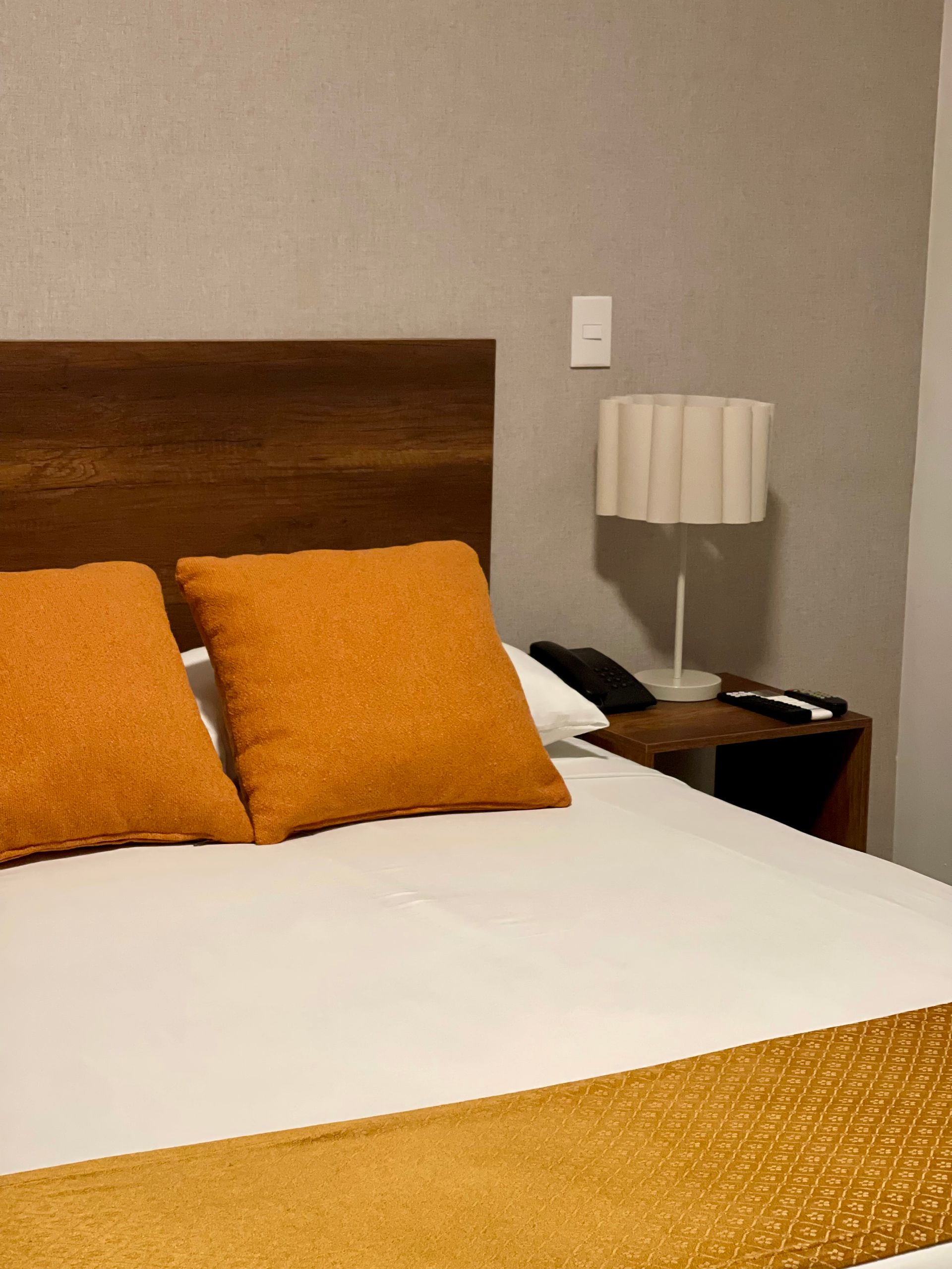 A bedroom featuring a bed with white sheets, two mustard yellow square pillows, and a matching runner on a wooden bed frame.