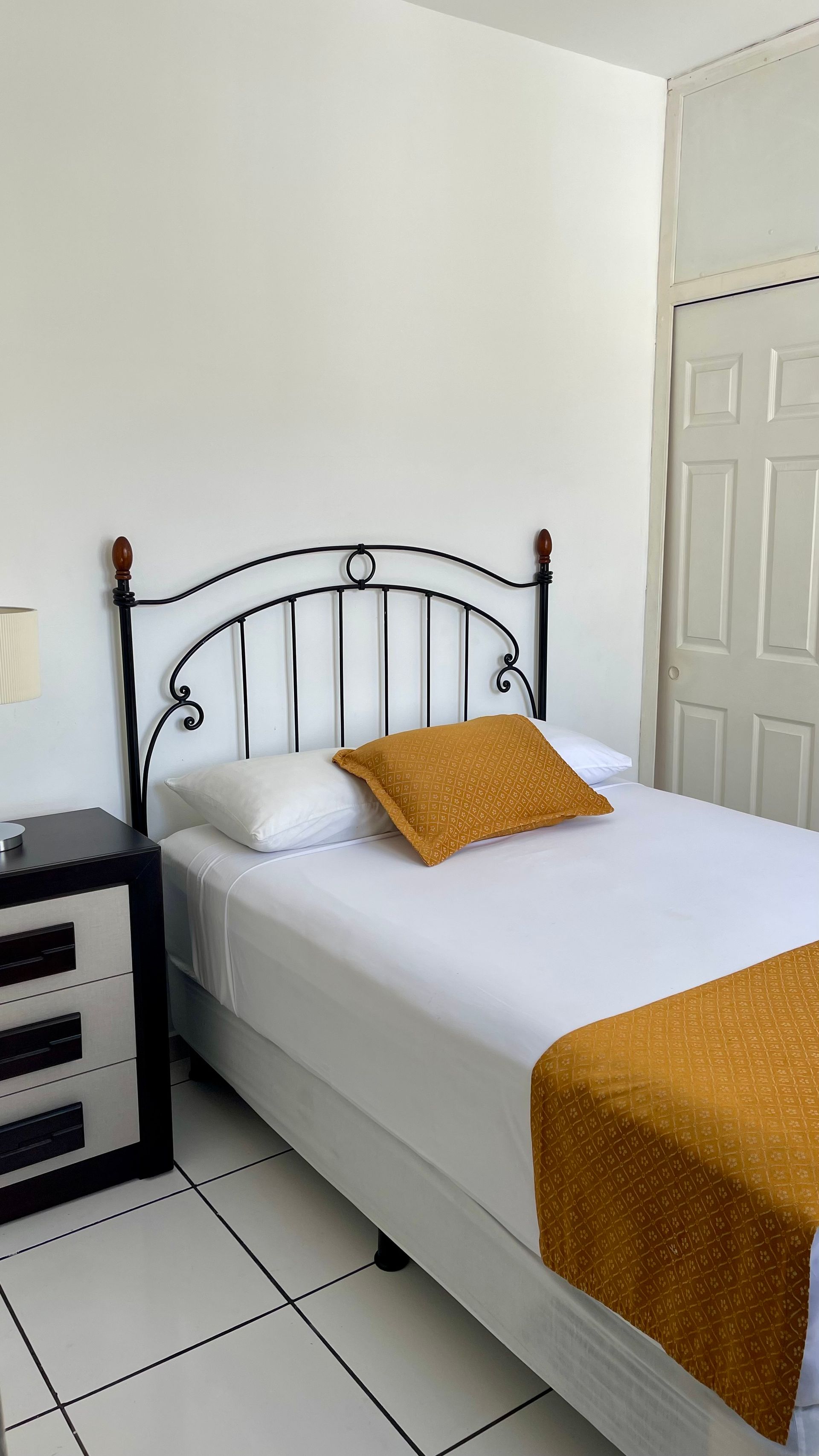 A bedroom featuring a bed with a black metal frame, white bedding, and a gold textured pillow and runner.