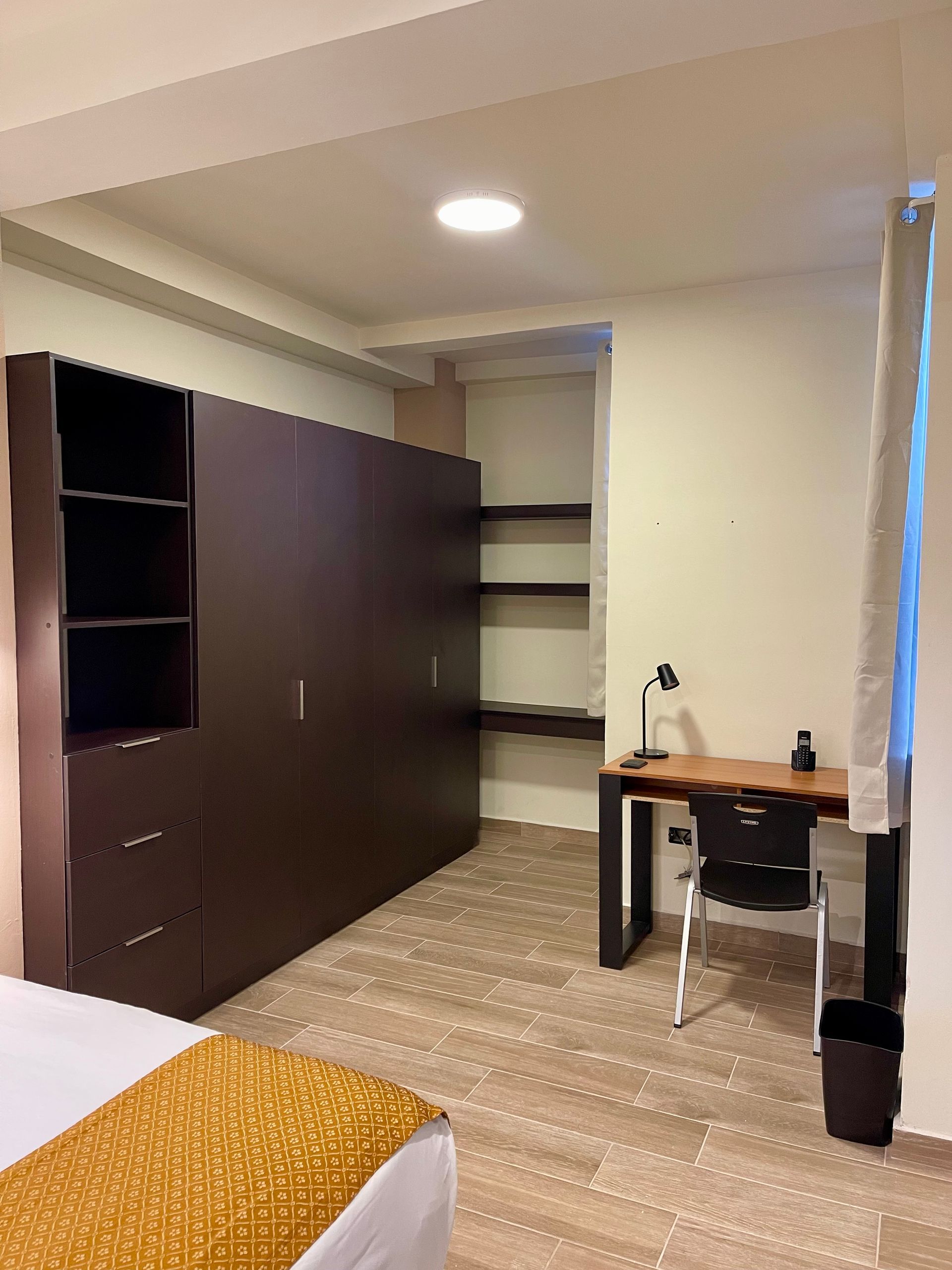 A bedroom with a bed , desk , chair and shelves.