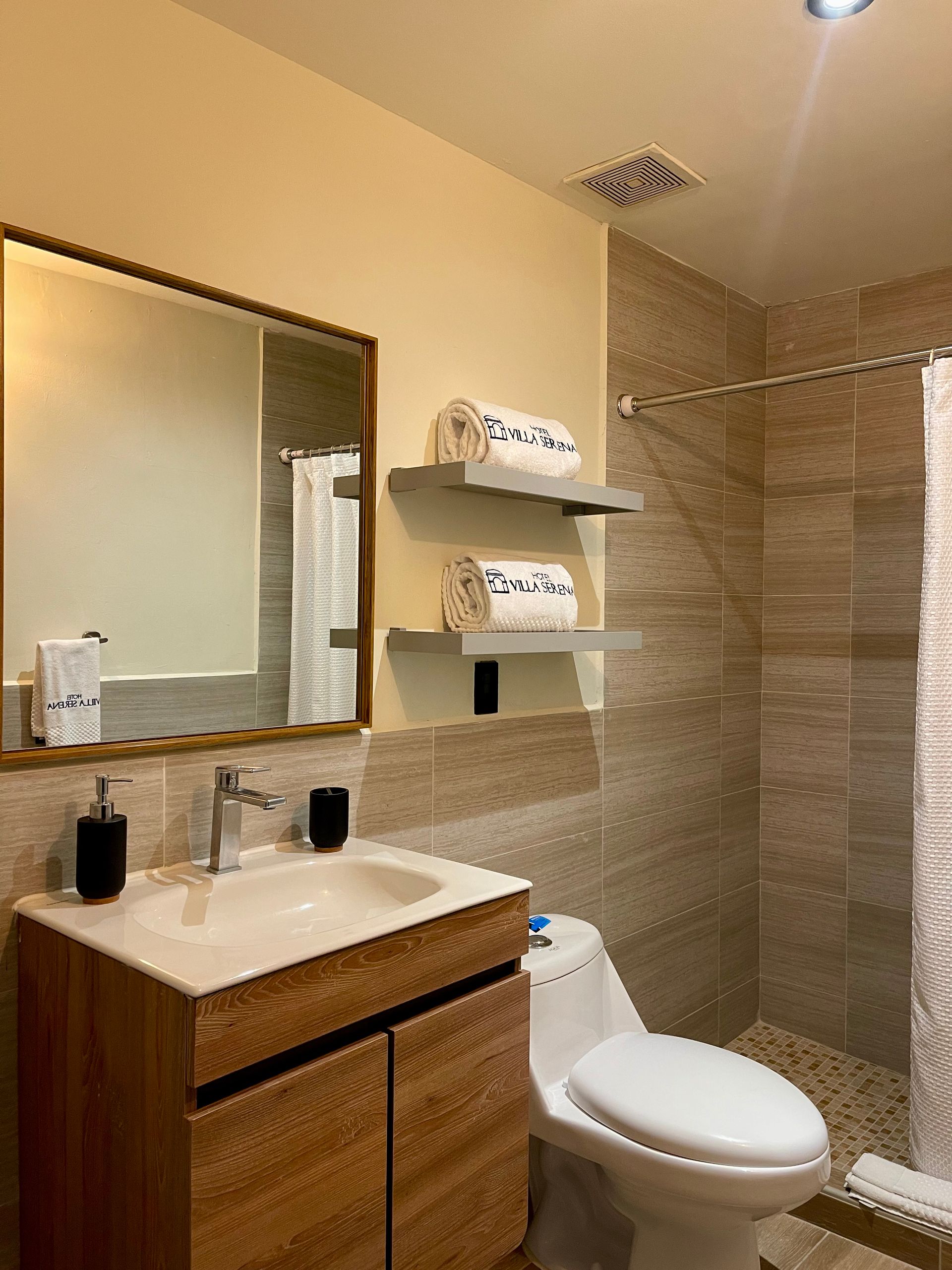 A bathroom with a toilet , sink , mirror and shower.