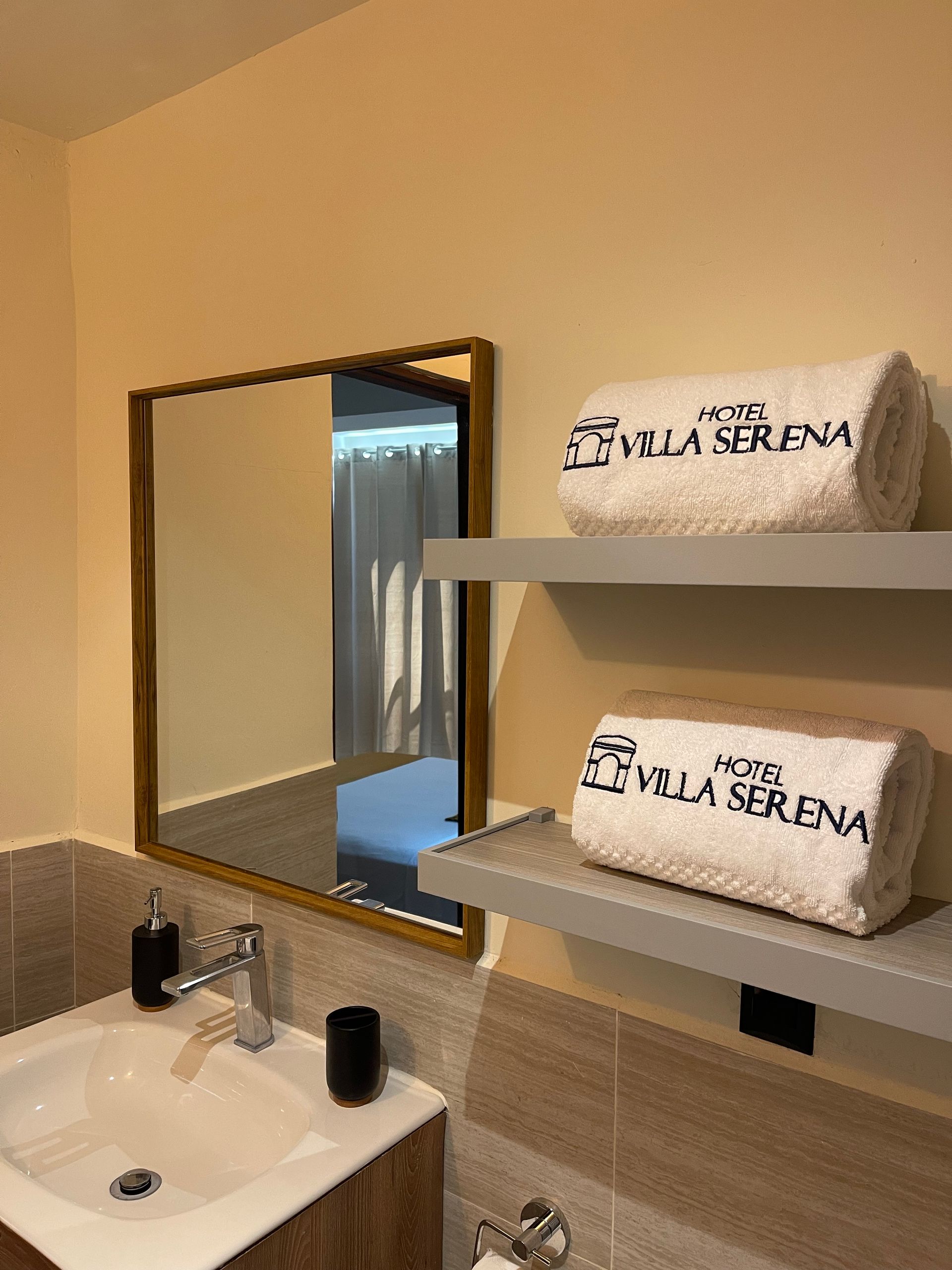 A bathroom with a sink , mirror , shelves and towels.